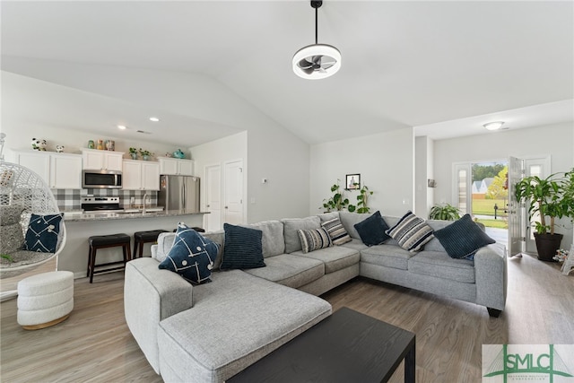 living room with light wood-type flooring, lofted ceiling, ceiling fan, and sink