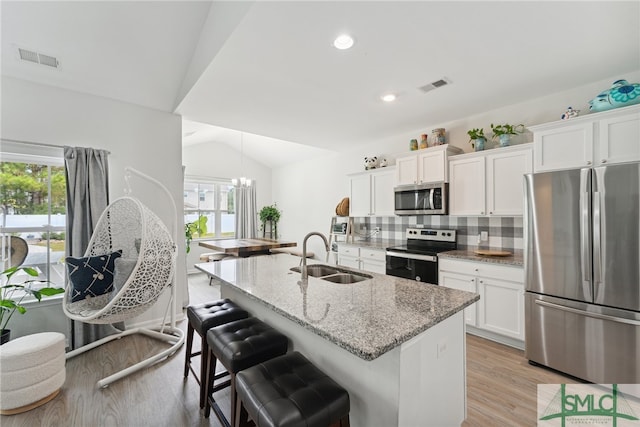 kitchen with sink, appliances with stainless steel finishes, white cabinets, light wood-type flooring, and vaulted ceiling