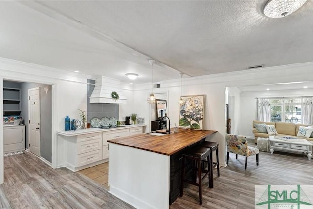 kitchen featuring custom exhaust hood, sink, washer / dryer, white cabinetry, and butcher block counters