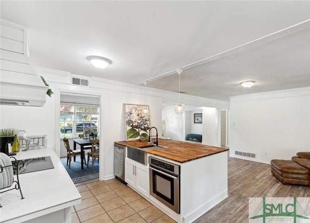 kitchen featuring stainless steel appliances, wood counters, kitchen peninsula, pendant lighting, and white cabinets