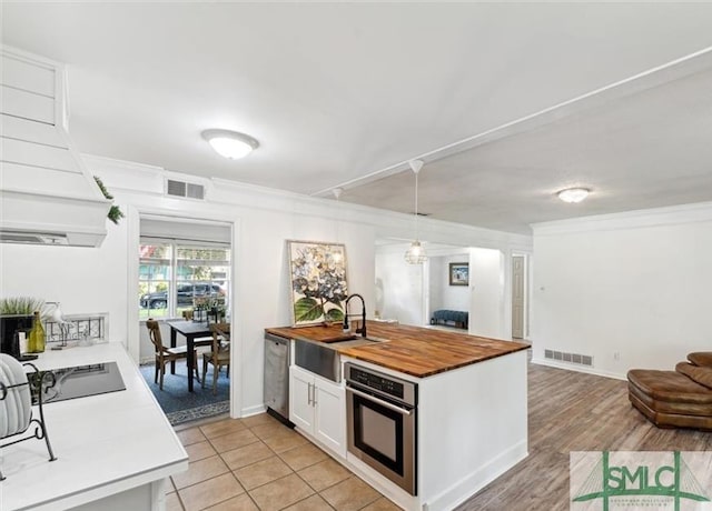 kitchen with butcher block counters, sink, pendant lighting, white cabinets, and appliances with stainless steel finishes