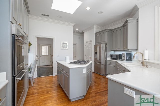 kitchen with light wood-style flooring, gray cabinetry, a sink, visible vents, and appliances with stainless steel finishes