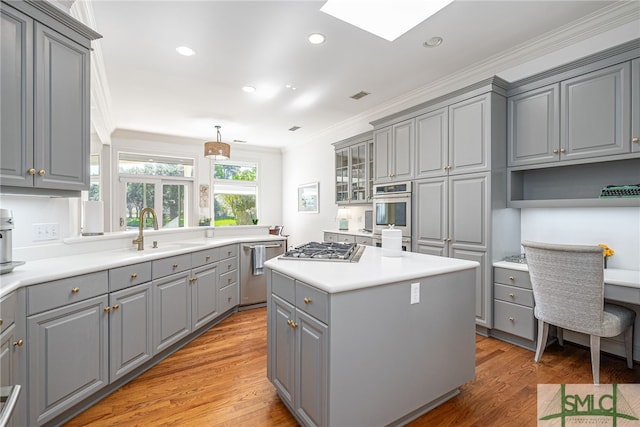 kitchen with a center island, stainless steel appliances, crown molding, gray cabinets, and a sink