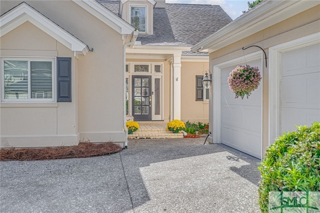 entrance to property featuring a garage, a shingled roof, and stucco siding