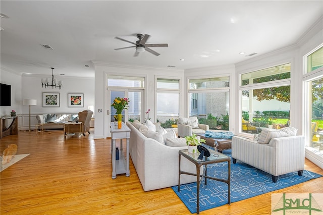 living area featuring ceiling fan with notable chandelier, ornamental molding, light wood-type flooring, and visible vents