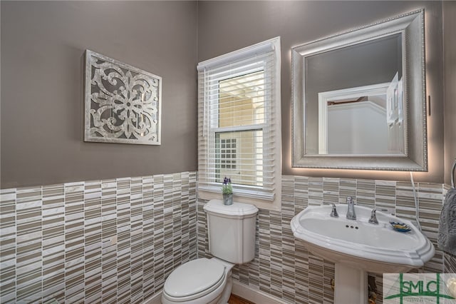 half bath with toilet, a wainscoted wall, a sink, and tile walls