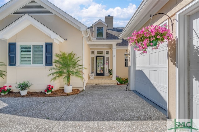 property entrance featuring concrete driveway, a chimney, a garage, and stucco siding