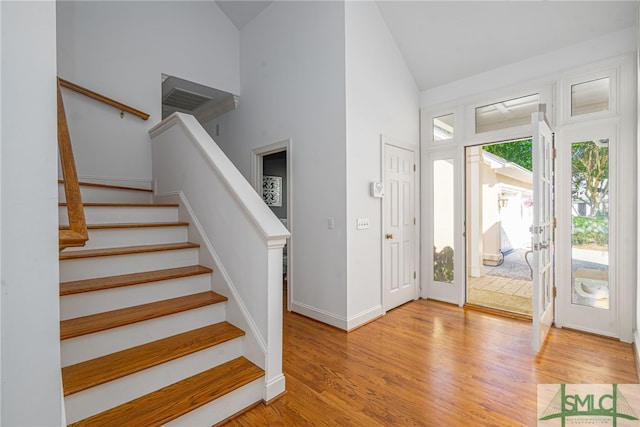 entryway with high vaulted ceiling, stairway, light wood finished floors, and baseboards