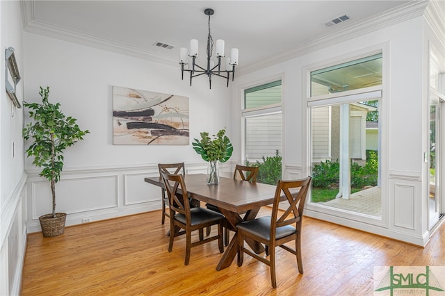 dining room with a chandelier, healthy amount of natural light, light wood-type flooring, crown molding, and a decorative wall