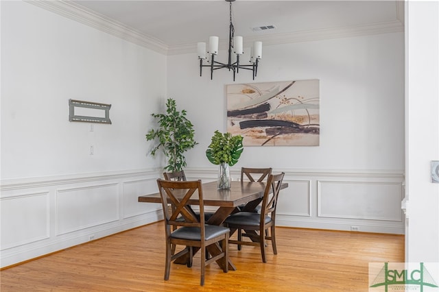 dining area featuring a chandelier, ornamental molding, wood finished floors, a wainscoted wall, and a decorative wall