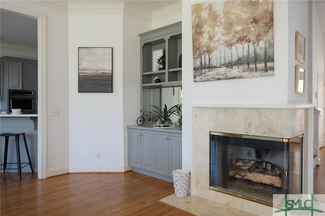 unfurnished living room with wood finished floors, ornamental molding, a high end fireplace, baseboards, and built in features