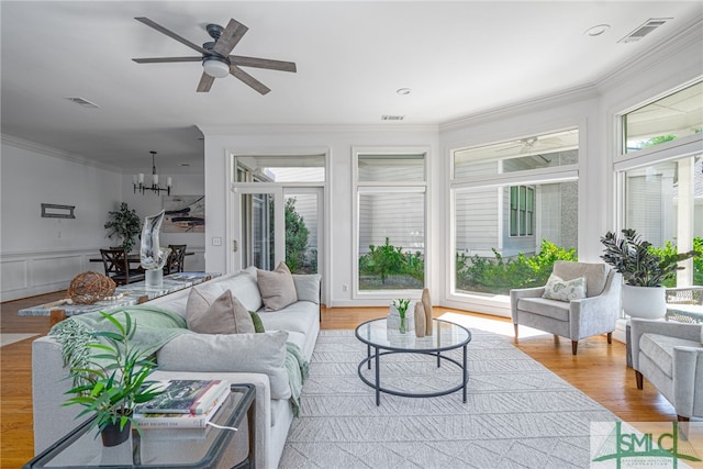 living room featuring healthy amount of natural light, ornamental molding, a chandelier, a ceiling fan, and wood finished floors
