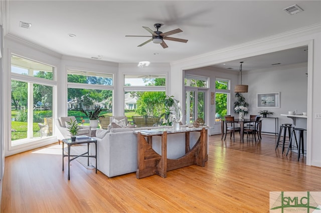 living area featuring healthy amount of natural light, ceiling fan, light wood-style flooring, and ornamental molding