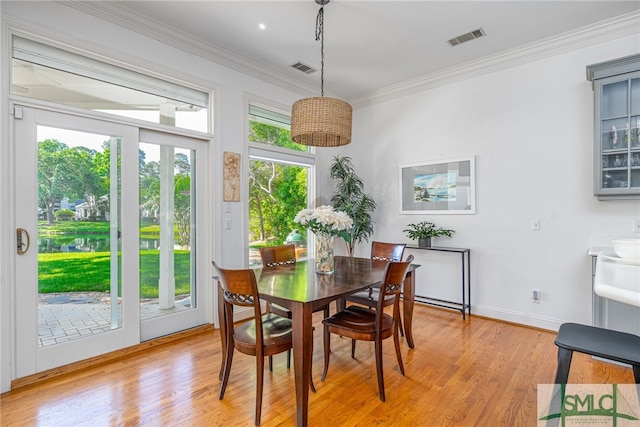 dining room featuring light wood-style flooring, ornamental molding, a water view, and baseboards