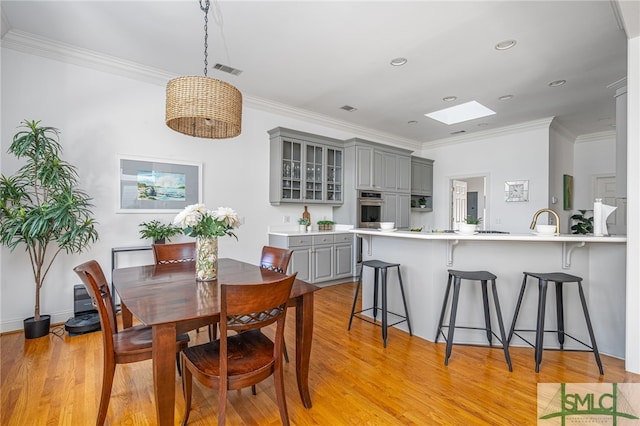 dining room featuring a skylight, light wood-type flooring, crown molding, and recessed lighting