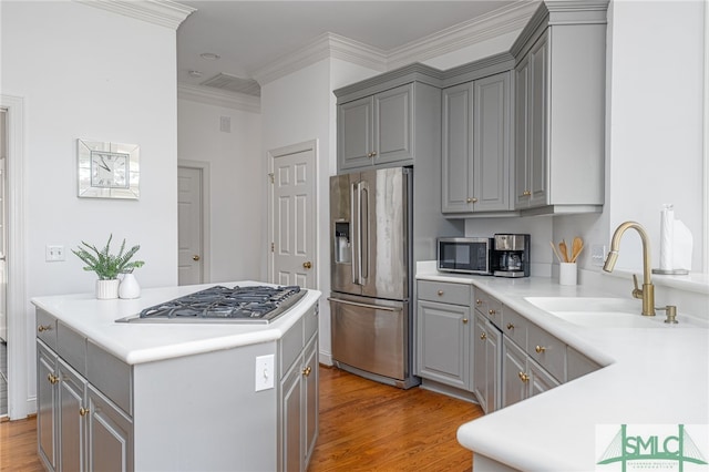 kitchen with gray cabinets, stainless steel appliances, a sink, light wood finished floors, and crown molding