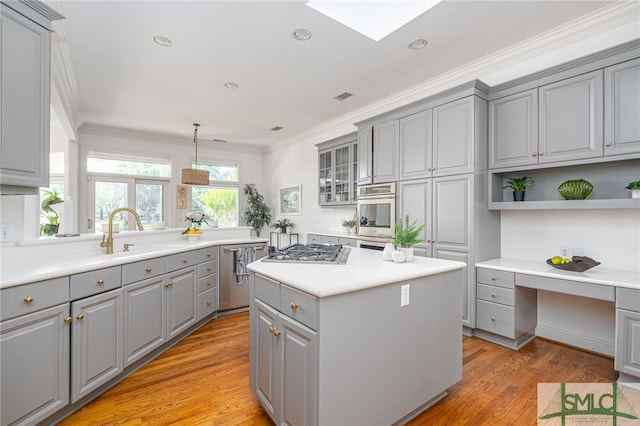 kitchen featuring gray cabinets, stainless steel appliances, a kitchen island, ornamental molding, and light wood-style floors