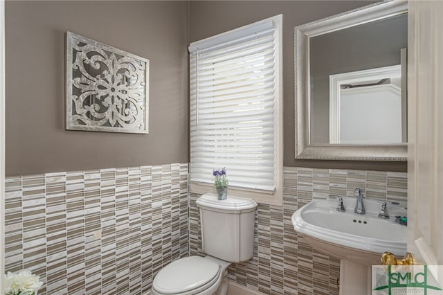 bathroom featuring tile walls, toilet, wainscoting, and a sink