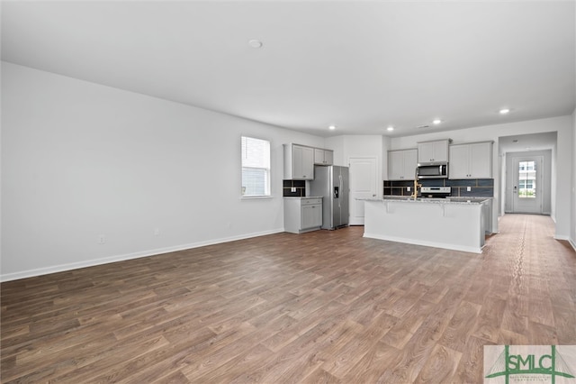 kitchen with light hardwood / wood-style flooring, appliances with stainless steel finishes, light stone counters, and a kitchen island with sink