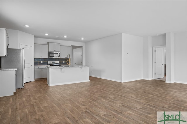 kitchen with tasteful backsplash, wood-type flooring, a center island with sink, stainless steel appliances, and sink