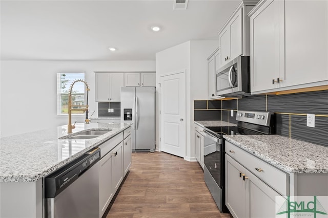 kitchen with wood-type flooring, stainless steel appliances, backsplash, sink, and an island with sink