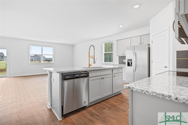 kitchen with dark hardwood / wood-style flooring, a center island with sink, light stone counters, sink, and appliances with stainless steel finishes