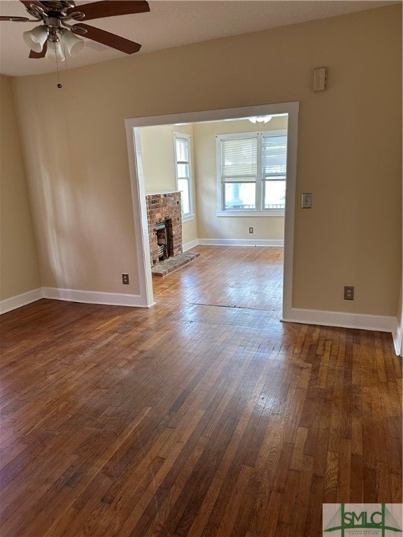 unfurnished living room featuring a fireplace, ceiling fan, and dark hardwood / wood-style flooring