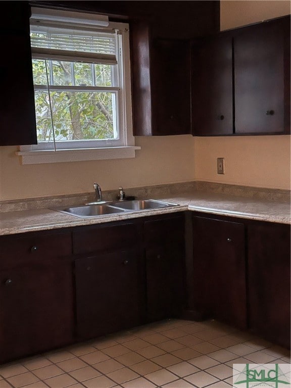 kitchen with dark brown cabinetry, sink, and light tile patterned flooring