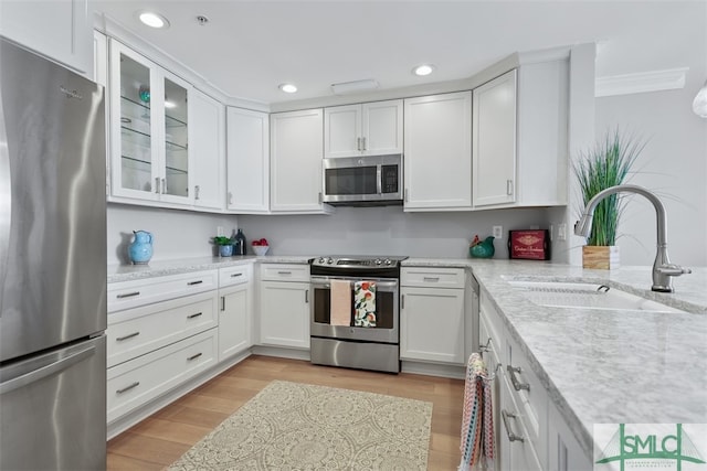 kitchen with sink, white cabinetry, light stone counters, light hardwood / wood-style flooring, and appliances with stainless steel finishes