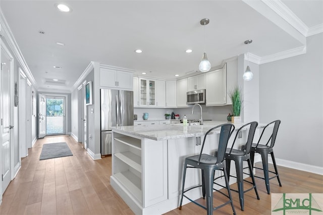 kitchen featuring white cabinets, hanging light fixtures, stainless steel appliances, crown molding, and light stone countertops