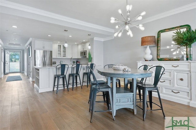 dining area with an inviting chandelier, ornamental molding, sink, and light wood-type flooring