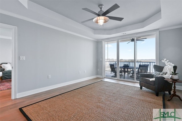 living area with crown molding, hardwood / wood-style flooring, a raised ceiling, and ceiling fan