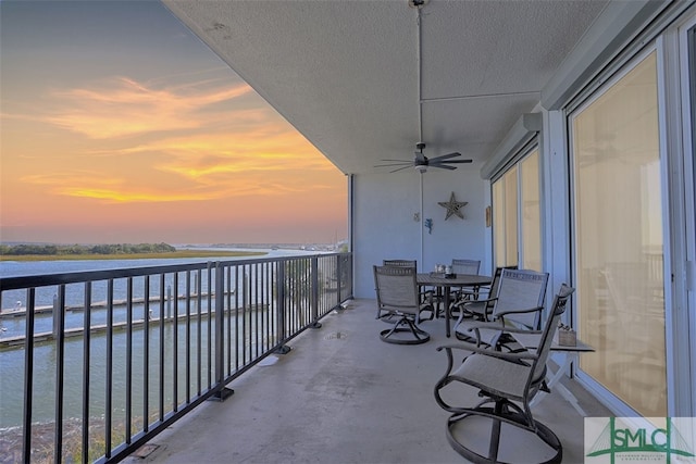 balcony at dusk featuring a water view and ceiling fan