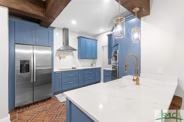 kitchen with stainless steel appliances, decorative light fixtures, sink, blue cabinets, and wall chimney exhaust hood