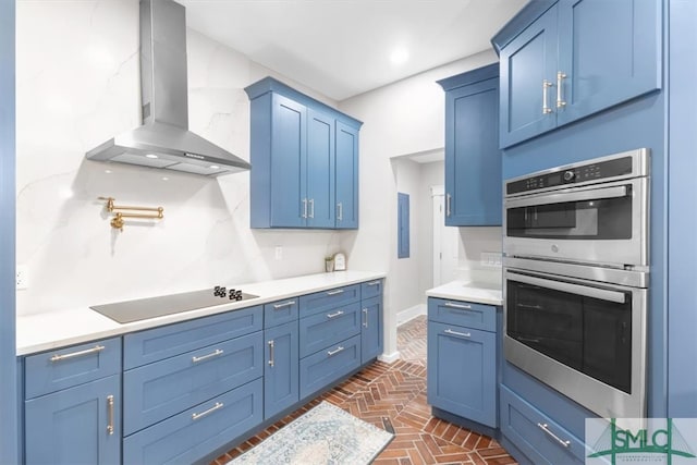 kitchen with stainless steel double oven, wall chimney exhaust hood, black electric stovetop, and blue cabinetry