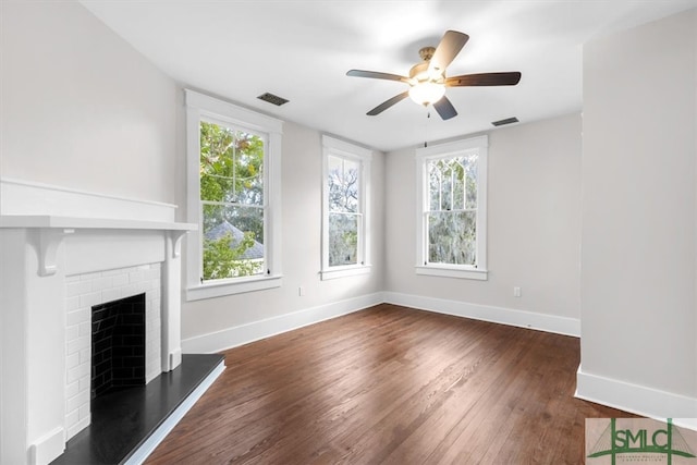 unfurnished living room featuring a fireplace, ceiling fan, dark hardwood / wood-style floors, and plenty of natural light