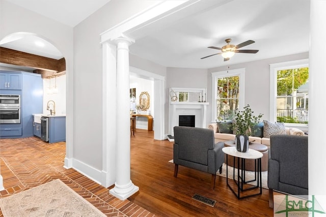 living room with dark wood-type flooring, decorative columns, ceiling fan, and beamed ceiling