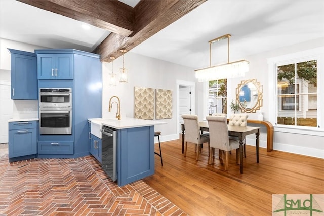 kitchen featuring pendant lighting, stainless steel appliances, beamed ceiling, and a healthy amount of sunlight