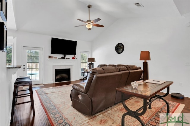 living room featuring ceiling fan, wood-type flooring, a tile fireplace, and high vaulted ceiling