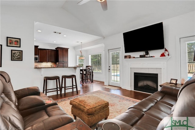 living room featuring hardwood / wood-style floors, a tiled fireplace, vaulted ceiling, and a healthy amount of sunlight