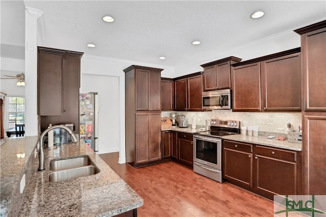 kitchen with ornamental molding, stainless steel appliances, light stone countertops, sink, and light hardwood / wood-style floors