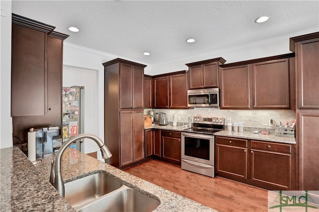 kitchen with stainless steel appliances, light hardwood / wood-style floors, sink, light stone counters, and tasteful backsplash