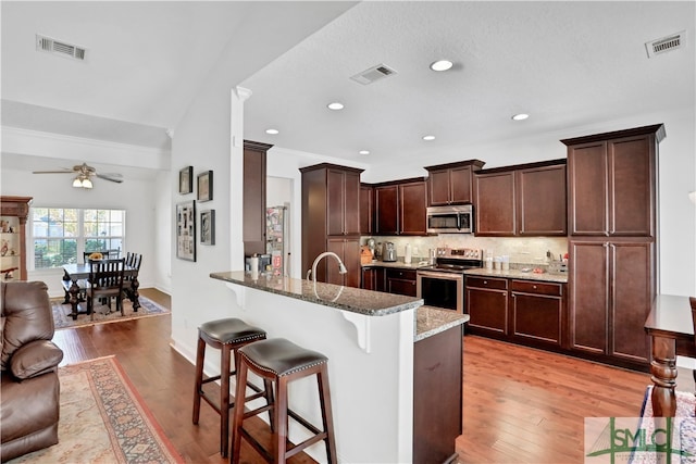 kitchen featuring a breakfast bar, kitchen peninsula, appliances with stainless steel finishes, stone counters, and light hardwood / wood-style flooring