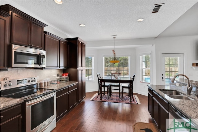 kitchen with light stone counters, sink, dark hardwood / wood-style floors, appliances with stainless steel finishes, and decorative light fixtures