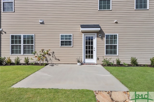 view of exterior entry with a lawn and a patio