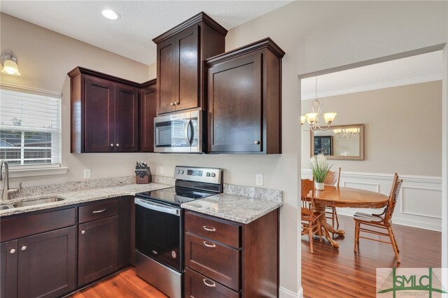 kitchen with light hardwood / wood-style floors, sink, appliances with stainless steel finishes, light stone countertops, and a chandelier