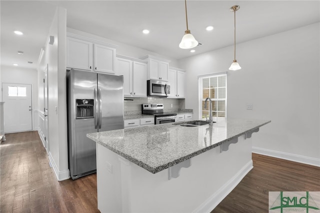 kitchen featuring white cabinets, pendant lighting, appliances with stainless steel finishes, dark wood-type flooring, and light stone counters