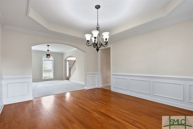 empty room with wood-type flooring, a raised ceiling, a chandelier, and crown molding