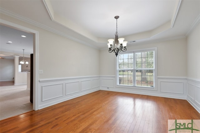 unfurnished room with an inviting chandelier, a tray ceiling, hardwood / wood-style floors, and ornamental molding