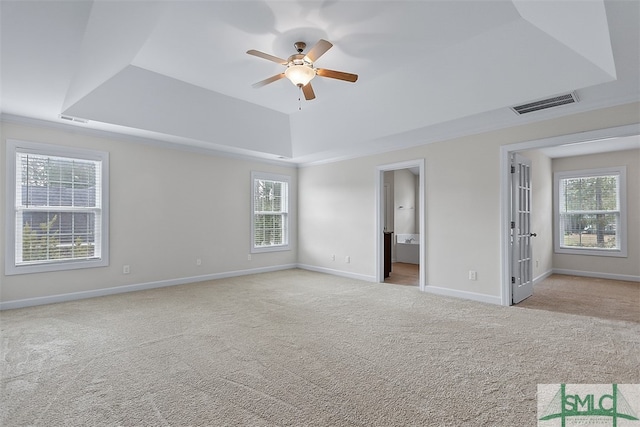 empty room featuring a wealth of natural light, ceiling fan, light carpet, and a tray ceiling